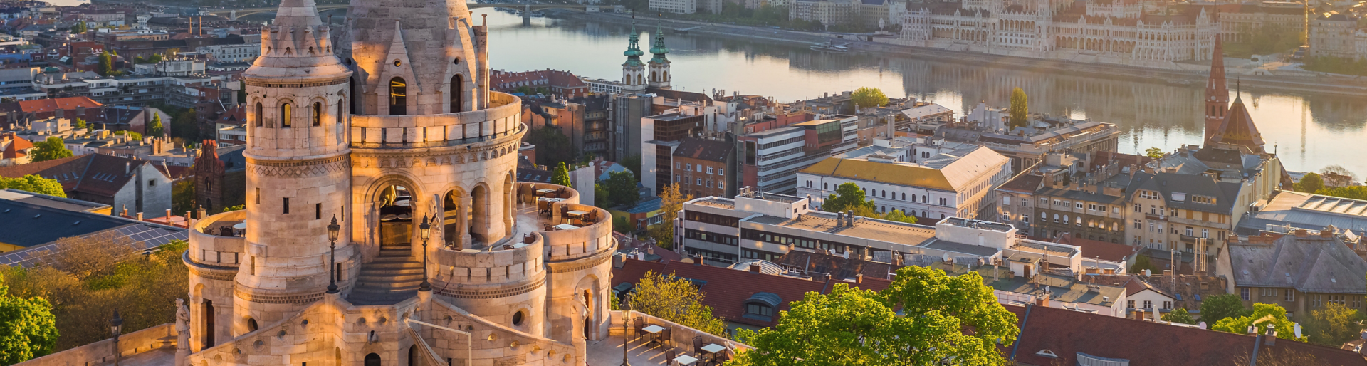 Budapest, Hungary - Beautiful golden summer sunrise with the tower of Fisherman's Bastion and green trees. Parliament of Hungary and River Danube at background. Blue sky.