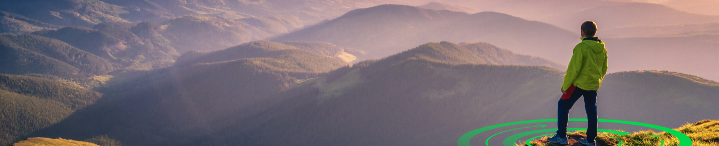 Sporty man on the mountain peak looking on mountain valley with sunbeams at colorful sunset in autumn in Europe. Landscape with traveler, foggy hills, forest in fall, amazing sky and sunlight in fall