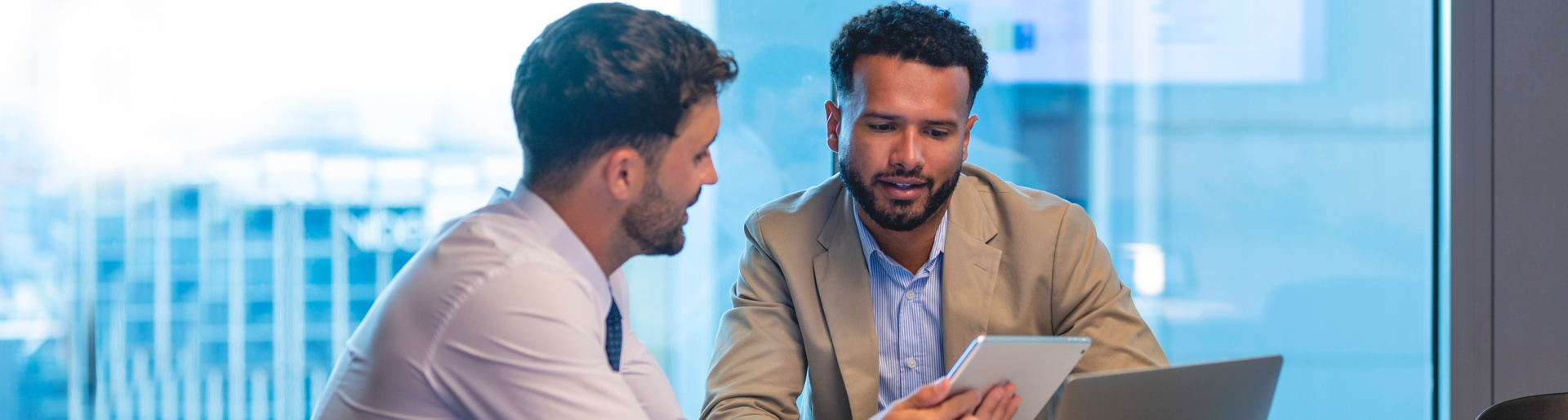 Business people working on a digital tablet and laptop. One looks like the manager working with an employee, or a financial advisor. It may also be a training session.