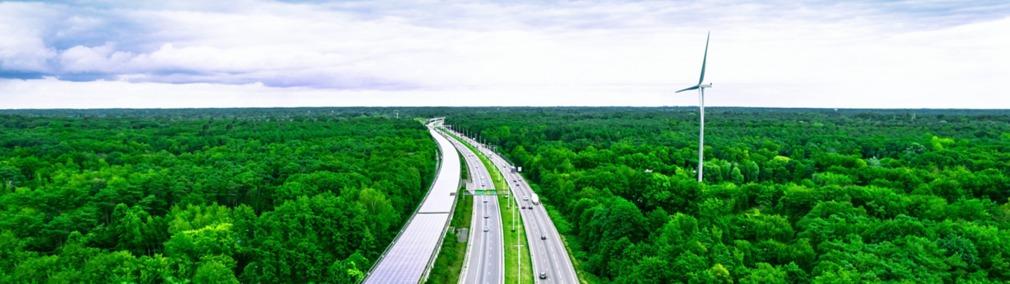 Aerial view taken with drone flying above multiple lane highway crossing luxuriant infinite forest with plain horizon, next to, the Peerdsbos railway tunnel covered with solar pannels with kilometers long. Antwerp. Belgium