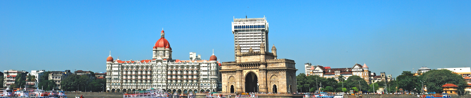 Wide angle panoramic view of Mumbai's famous heritage landmark Gateway of India as seen from the Arabian sea and busy sea front with colorful excursion ferry boats in foreground. Copy space.