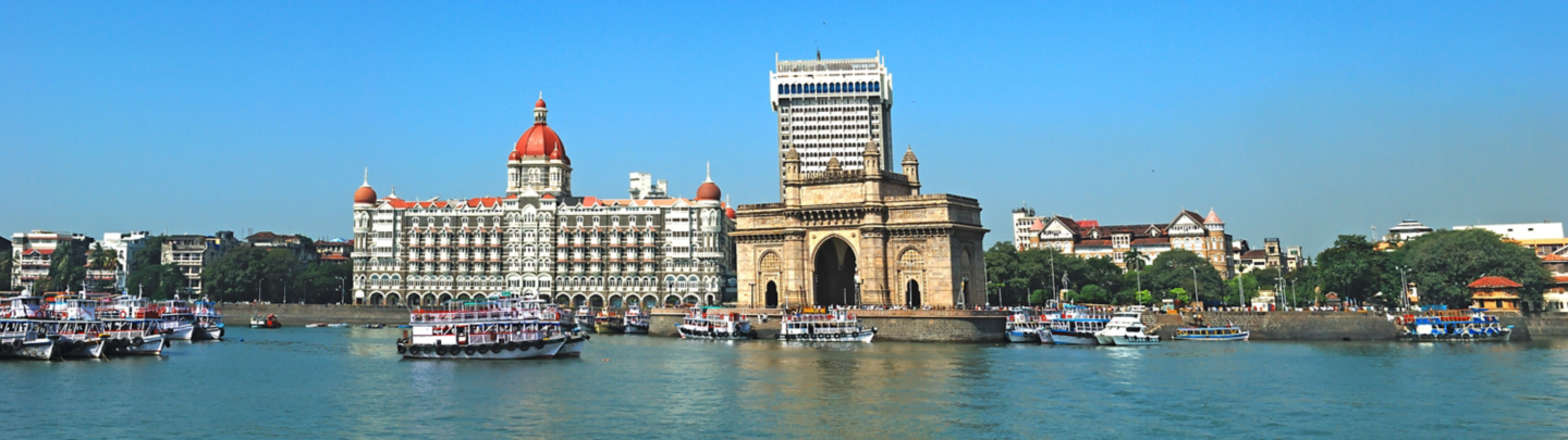 Wide angle panoramic view of Mumbai's famous heritage landmark Gateway of India as seen from the Arabian sea and busy sea front with colorful excursion ferry boats in foreground. Copy space.