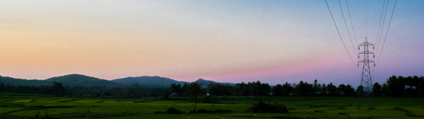 Power grid and power lines in green paddy fields in rural India. Mountain ranges seen at a distance. Colorful evening sky. Copy space for adding text.
